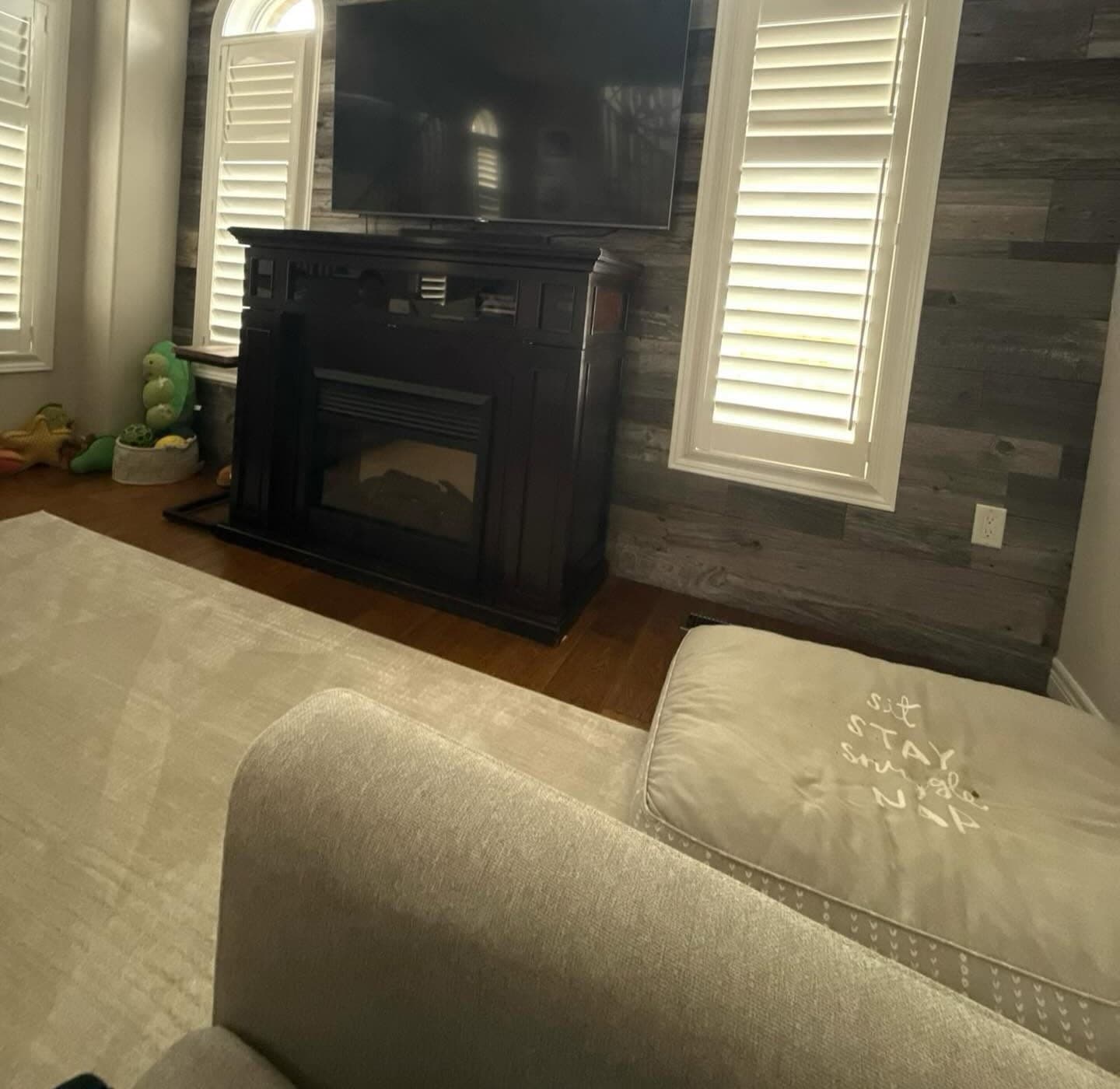 Living room before renovation with a dark fireplace cabinet and faux-wood accent wall